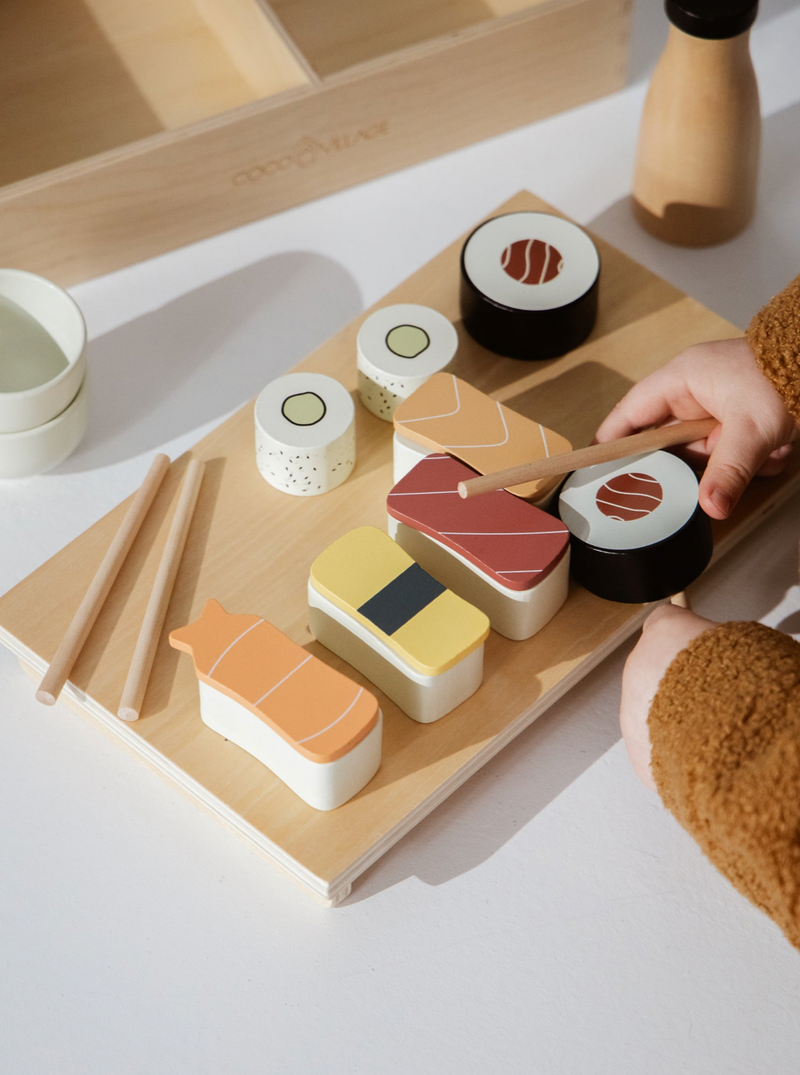 Wooden toy set of sushi on a wooden board with a hand holding chopsticks.