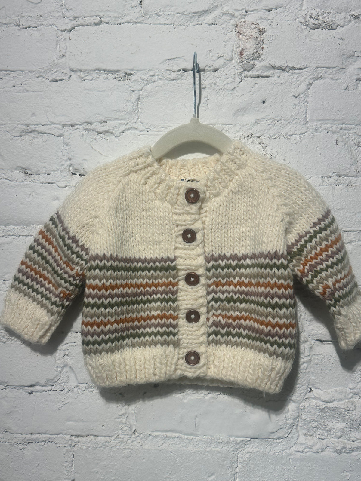 Knitted baby cardigan with striped pattern on a white brick wall background