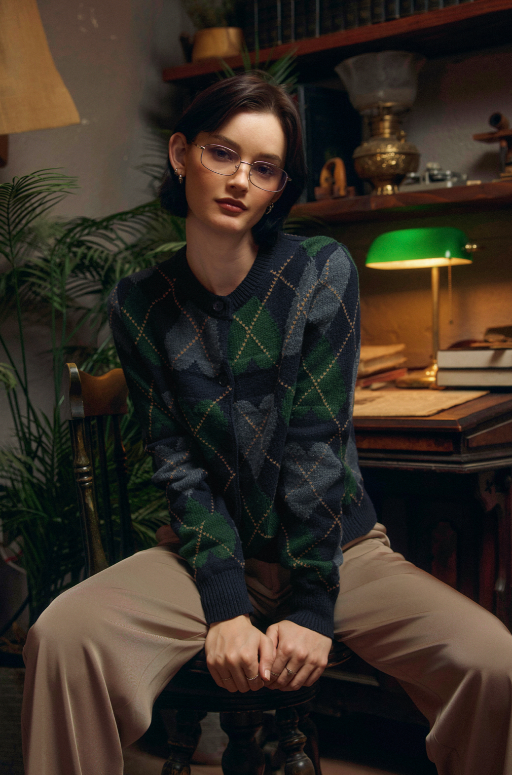 Person wearing a patterned sweater sitting in a room with books and lamps.