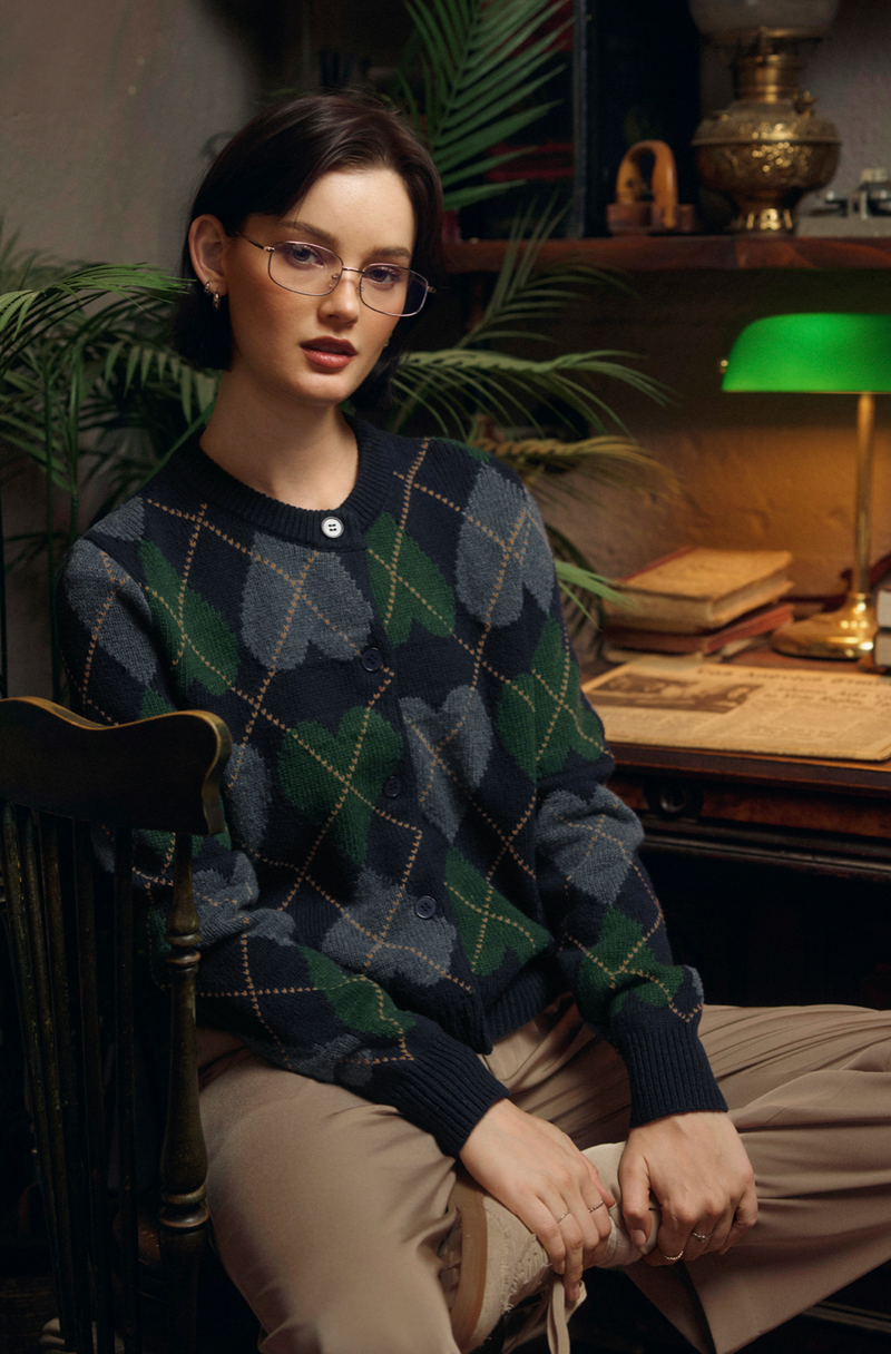 Woman wearing a patterned sweater sitting in a room with a desk and lamp.