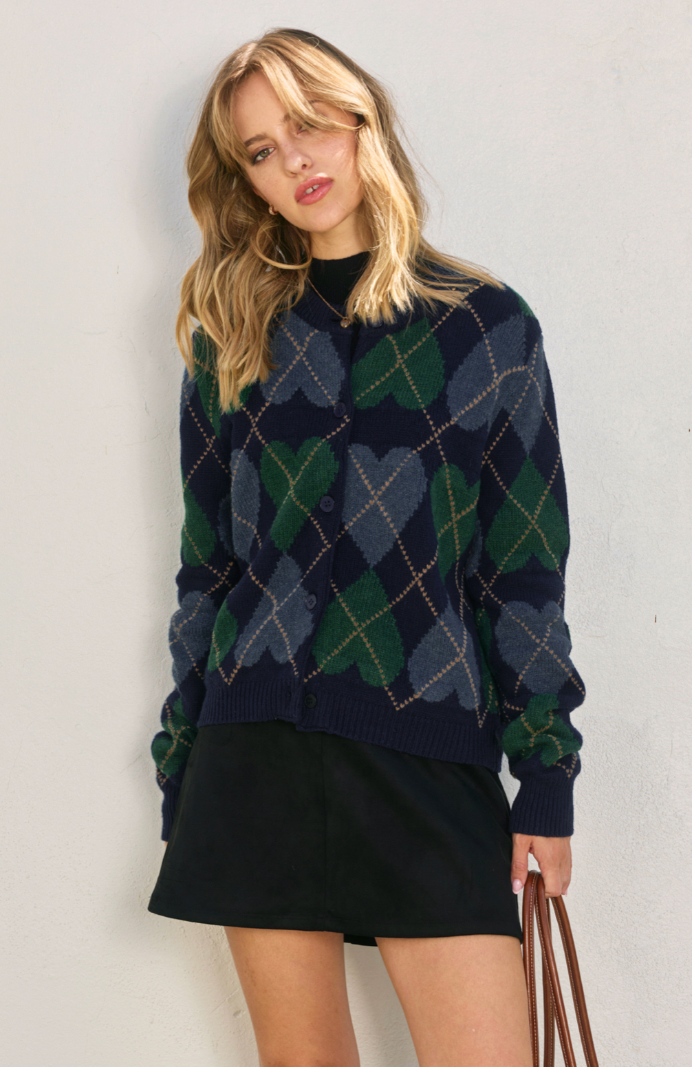 Woman wearing a navy and green argyle sweater with a plain background