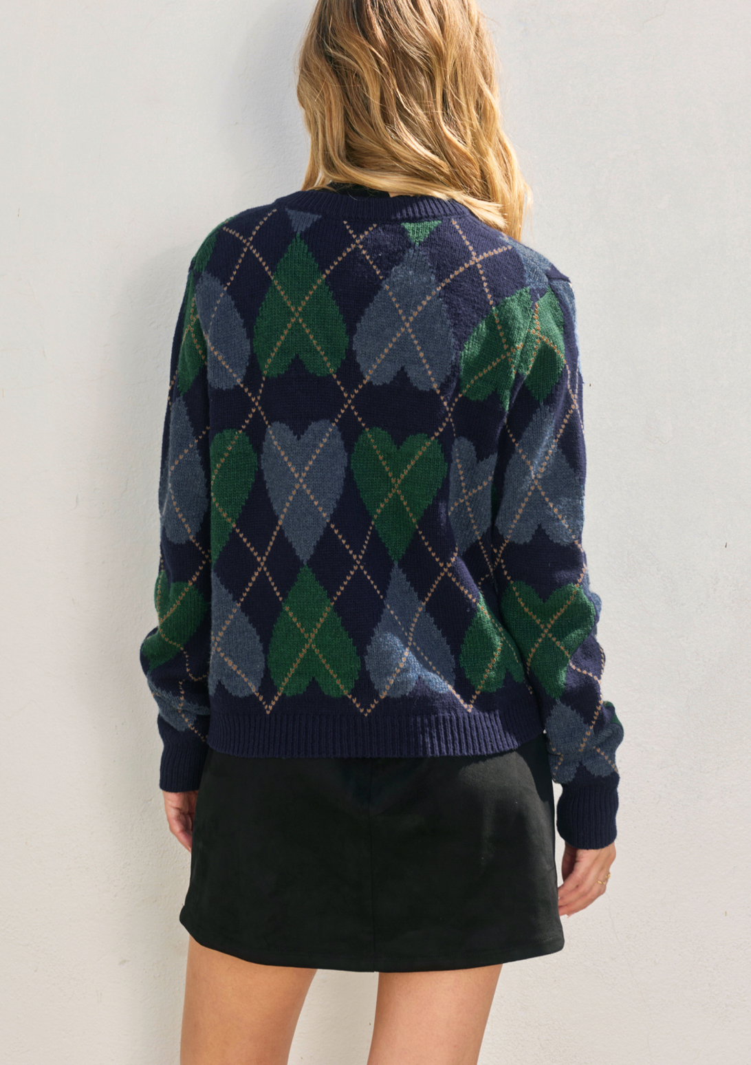 Person wearing a navy and green argyle sweater against a light background
