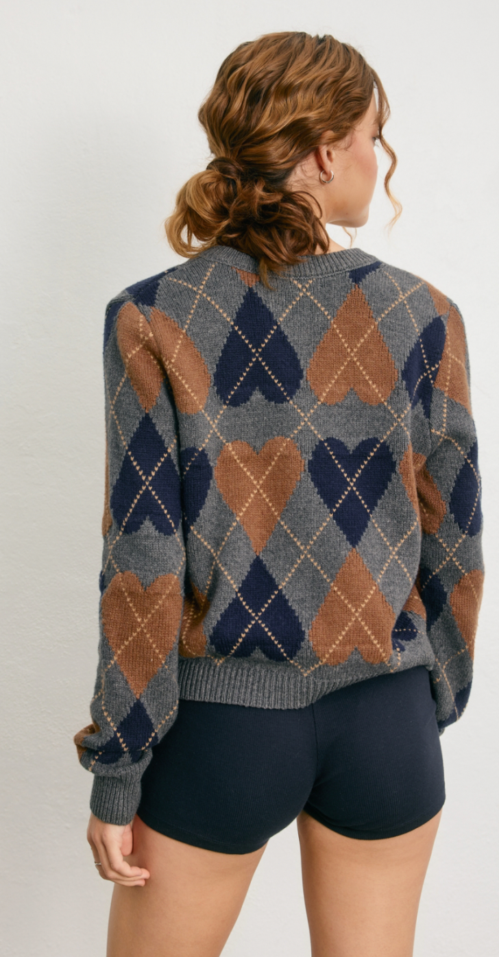 Person wearing a patterned sweater with hearts on a plain background