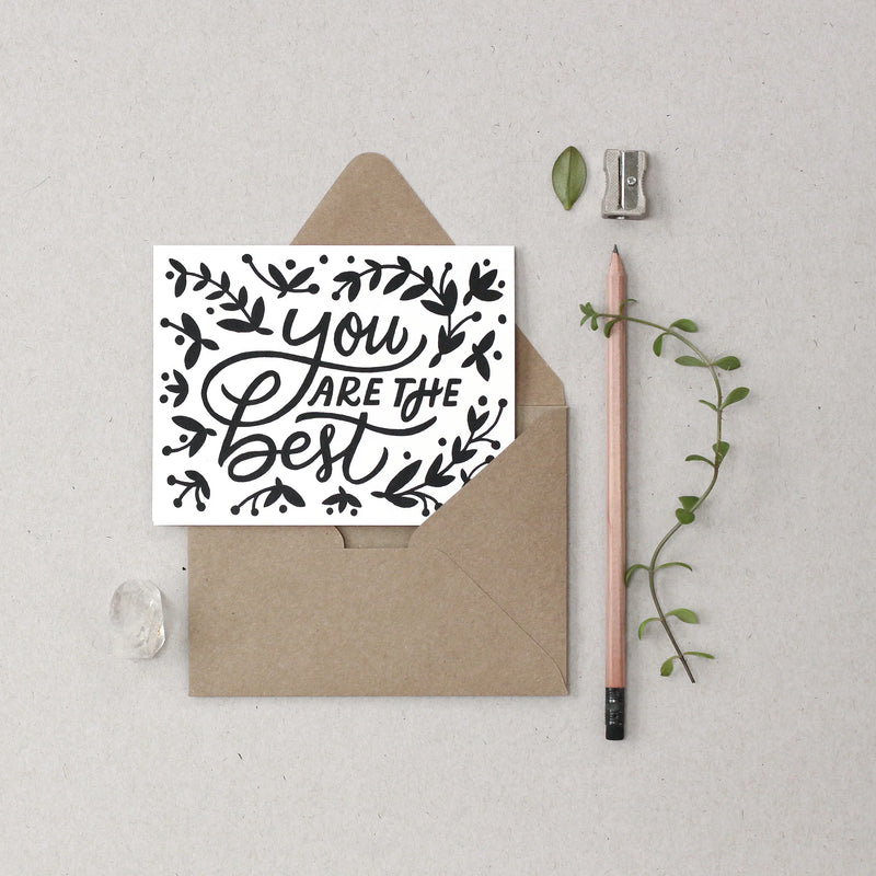 Card with 'You are the best' text on a beige envelope with a pencil and plant on a light gray background
